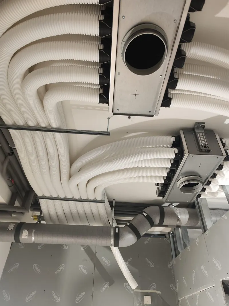 Vzduchotechnické rozdeľovacie boxy a biele potrubia vedené pod stropom